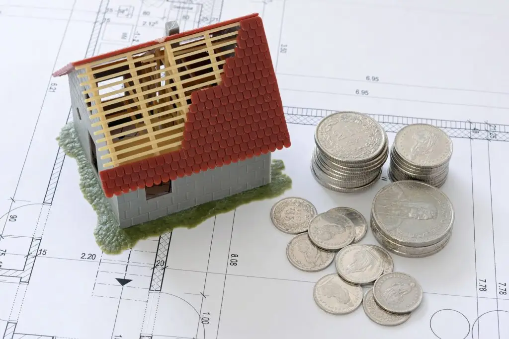 Coins and foreclosure property model sitting on a building blueprint