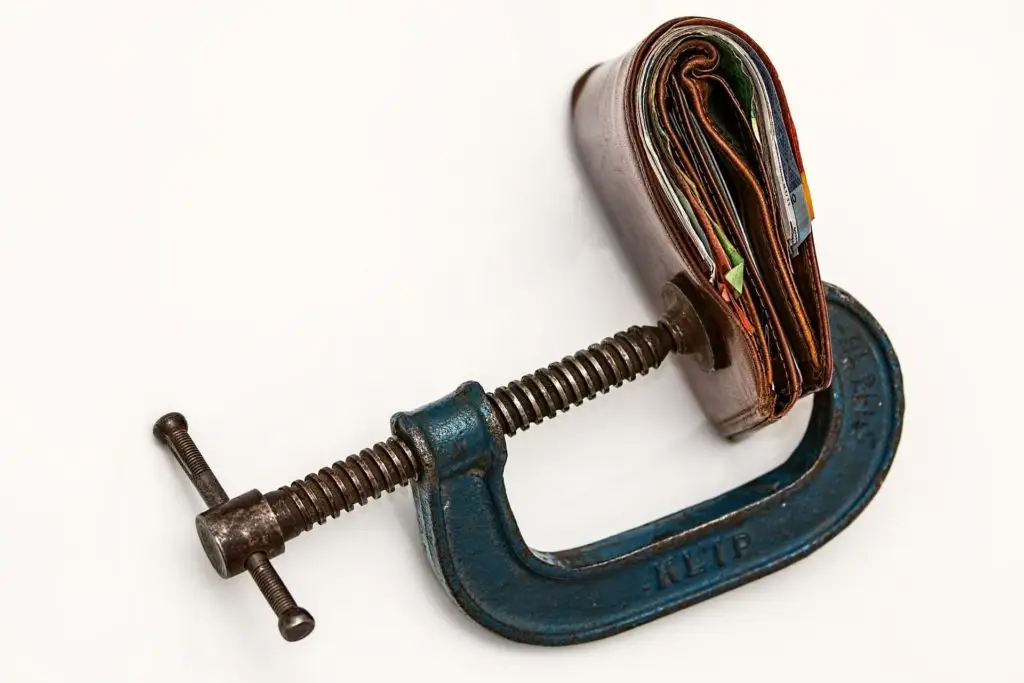Vice grip squeezing a wallet, illustrating financial pressure from missed mortgage payments