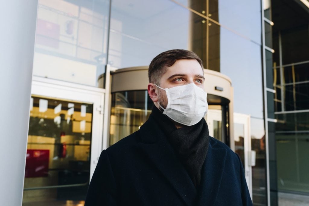 man walking out of apartment building with a surgical mask on for coronavirus